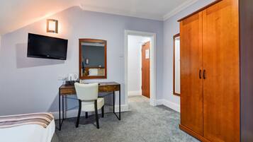 A hotel room with a bed, a desk with a chair, a television, a wardrobe, and a mirror.