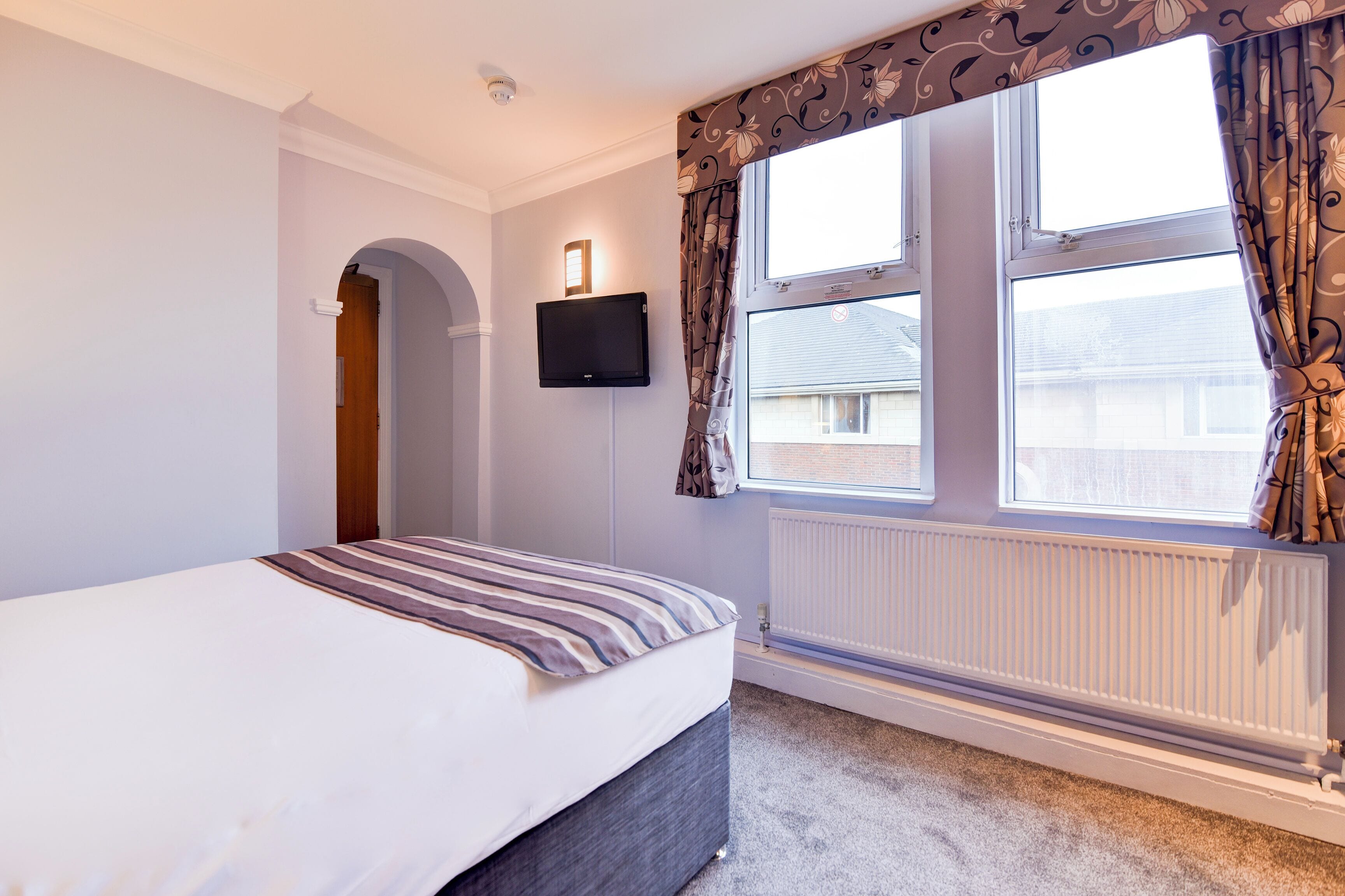 A bedroom with a bed, a TV mounted on the wall, and a window with curtains.