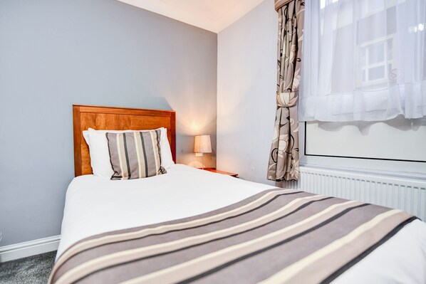 A neatly made bed with a striped blanket, a wooden headboard, and a bedside lamp.