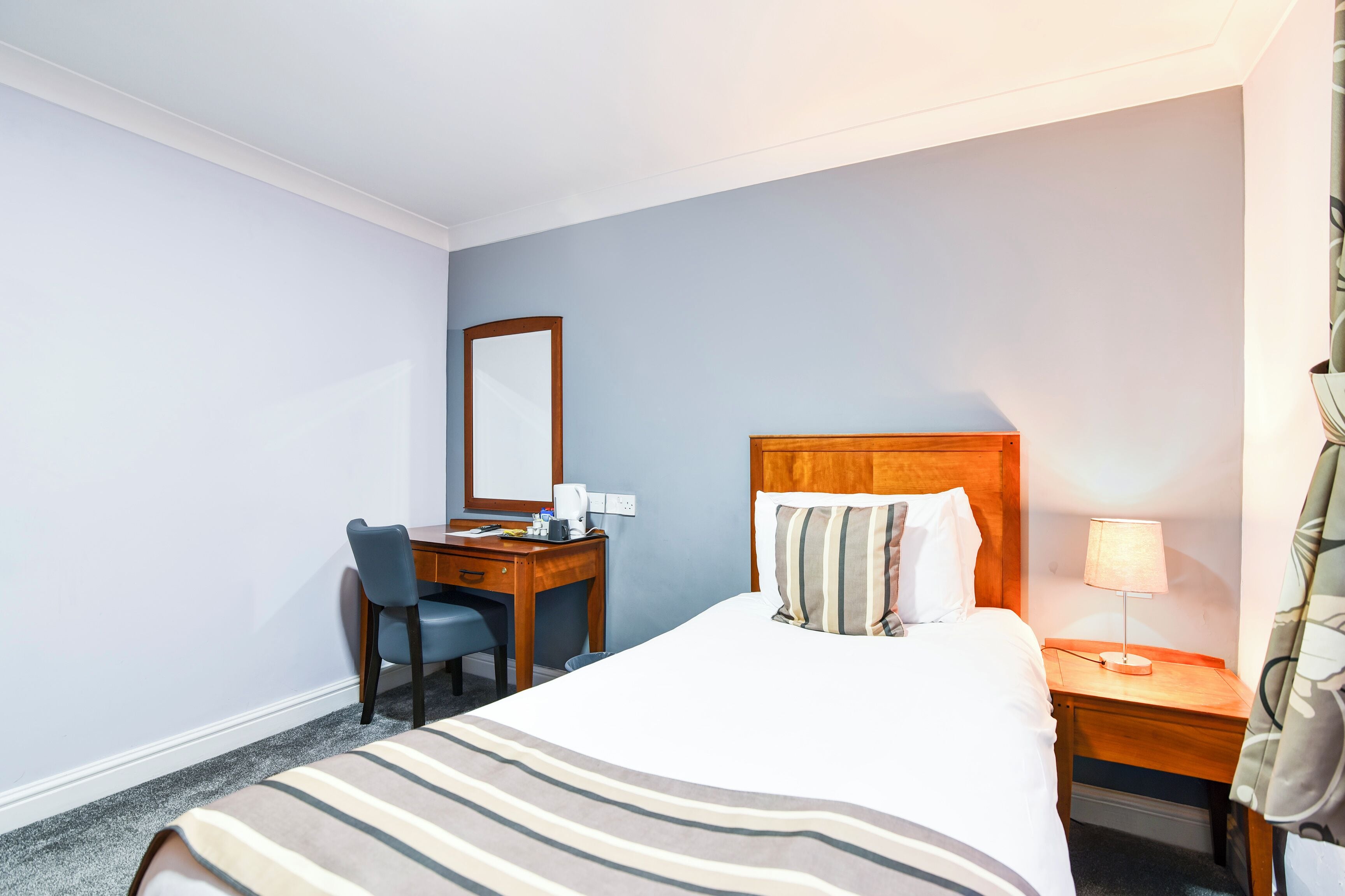 Une chambre d’hôtel avec un lit, un bureau, une chaise, une lampe et un miroir.