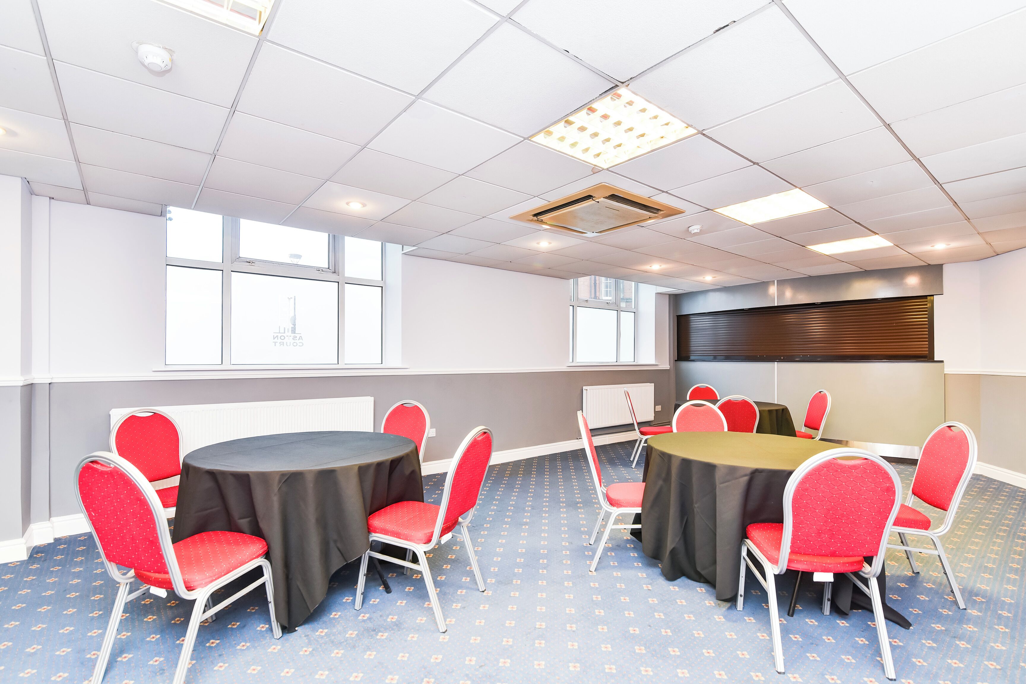 Un salón de conferencias con mesas redondas, sillas rojas y una pantalla grande.