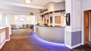A reception area with a curved counter, a reception desk, and a seating area with tables and chairs. - Aston Court Derby City Centre by Belvilla (Derby)