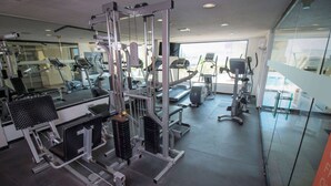 Ett gym med olika träningsmaskiner, en vägg med speglar och ett stort fönster som släpper in naturligt ljus.
