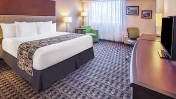 A hotel room with a large bed, two chairs, a desk with a television, and a window with curtains.