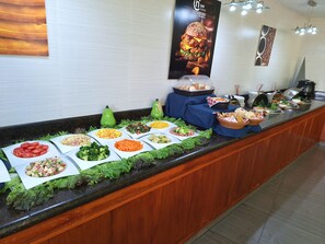 A buffet counter with various food items and a poster on the wall. - CHN Hotel Monterrey Norte, Trademark Collection by Wyndham (Monterrey)