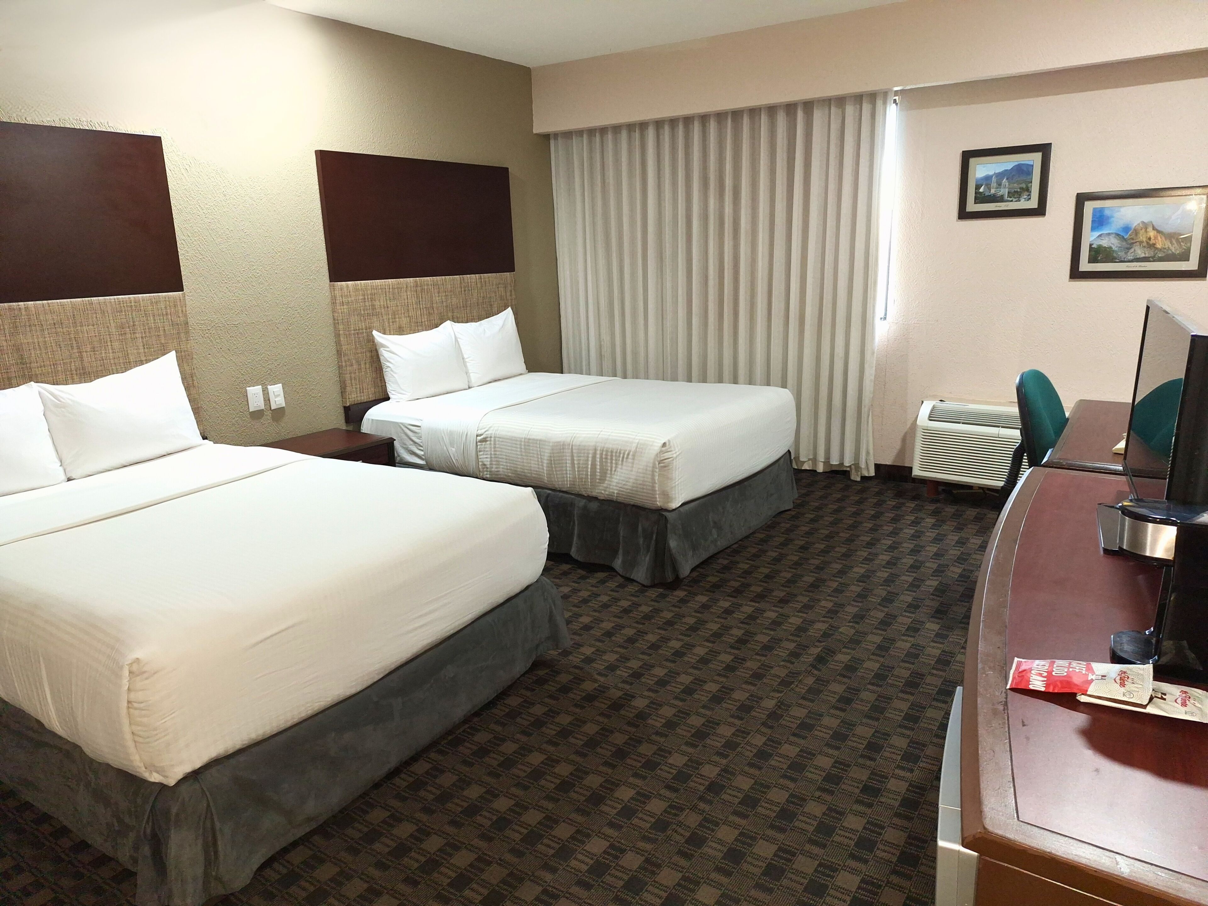 A hotel room with two beds, a desk with a television, and a window with curtains.