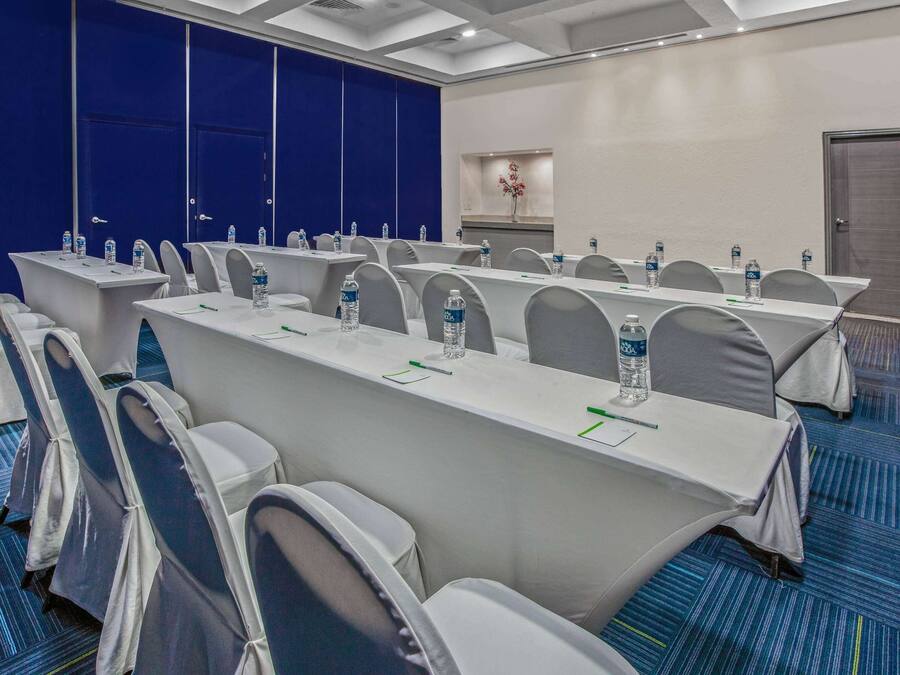 Un salón de conferencias con mesas largas, sillas y botellas de agua.