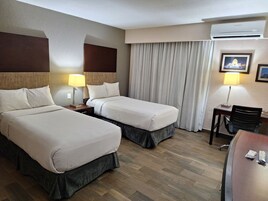 A hotel room with two beds, a desk, a chair, an air conditioning unit, and a television on the wall.
