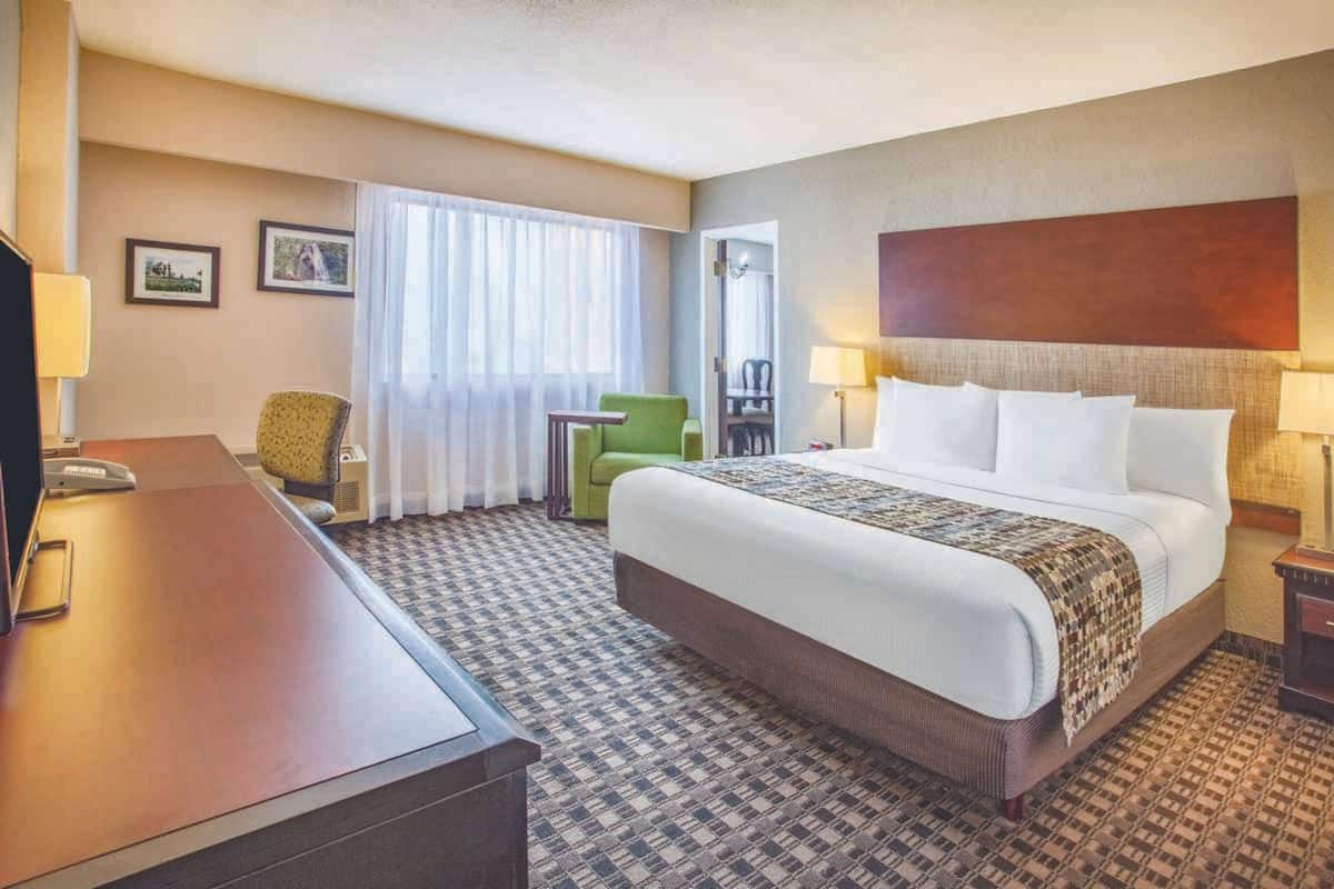 A hotel room with a large bed, a desk, a chair, and a small table.