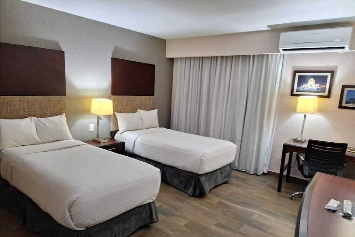 A hotel room with two beds, a desk, a chair, and an air conditioning unit.