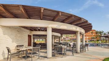 An outdoor patio area with tables and chairs, a pool, and a covered seating area with a curved roof.