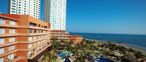 A hotel with a pool area, palm trees, and a beach view.