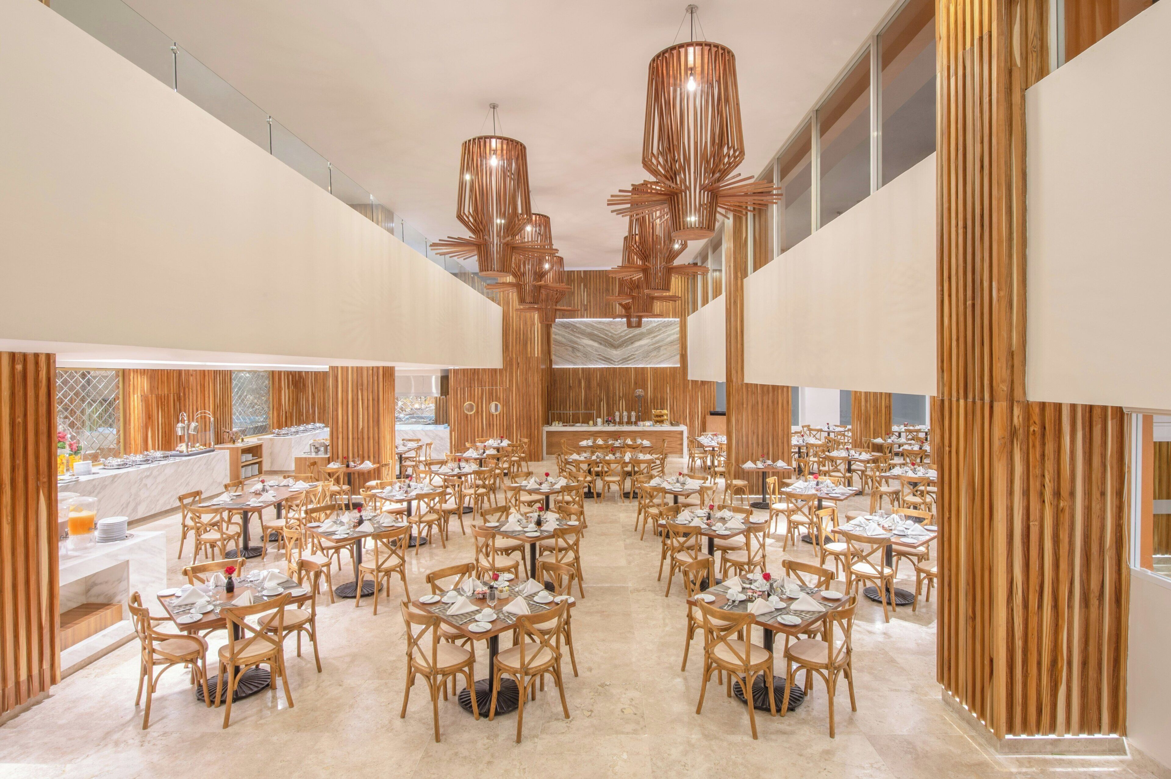 Een ruime eetruimte met meerdere tafels en stoelen, een centraal buffet en een moderne kroonluchter.