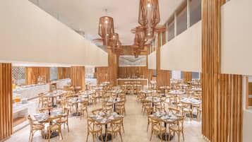 Een ruime eetruimte met meerdere tafels en stoelen, een centraal buffet en een moderne kroonluchter.