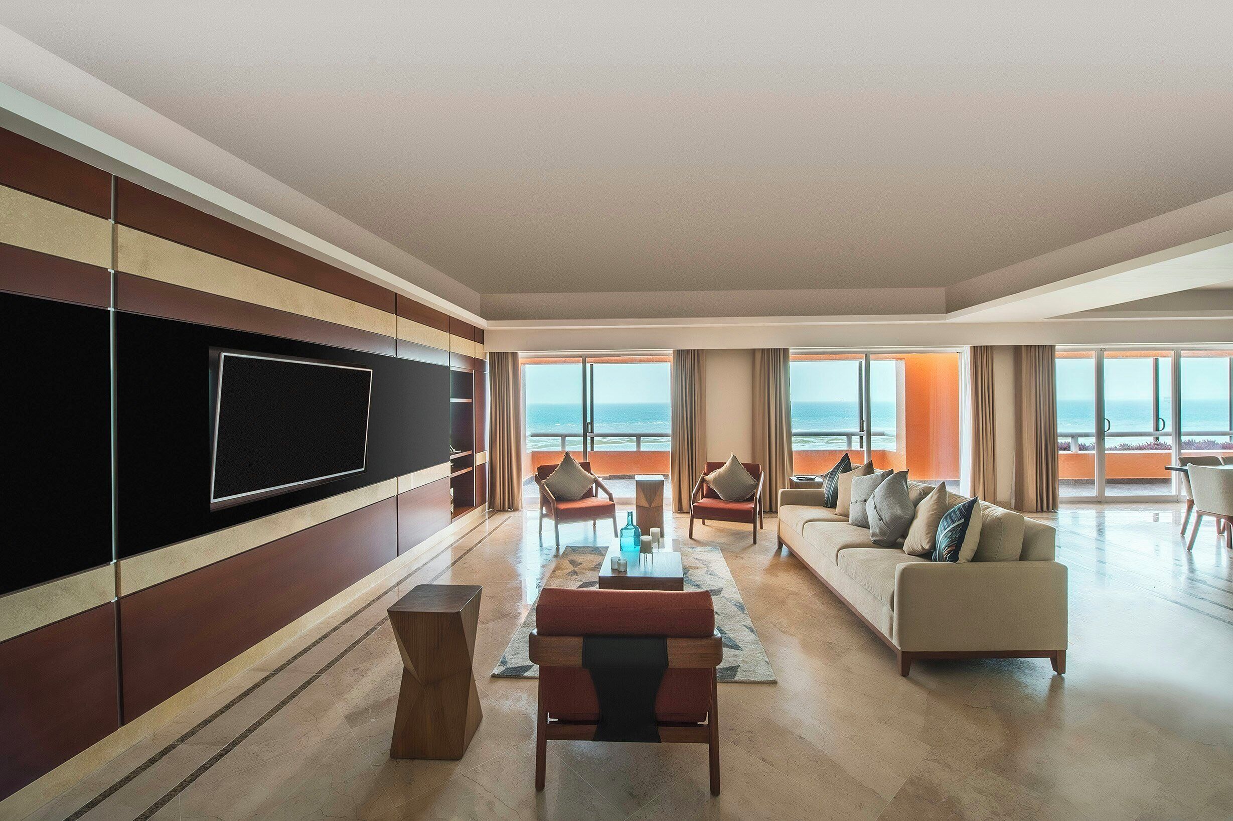 A spacious living room with a large flat-screen TV, a sofa, and chairs arranged around a coffee table.