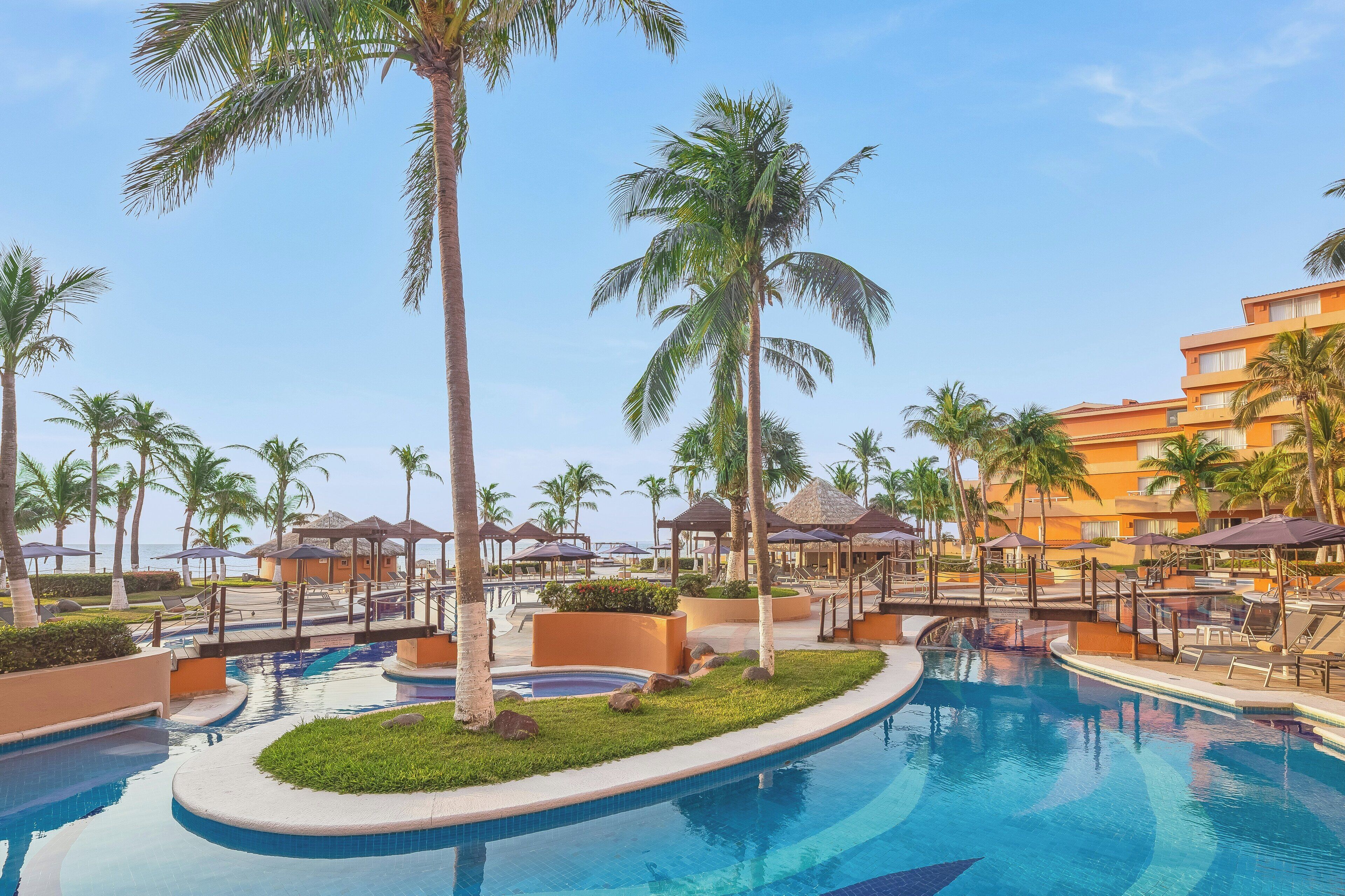 A resort pool area with palm trees, lounge chairs, and a building in the background.