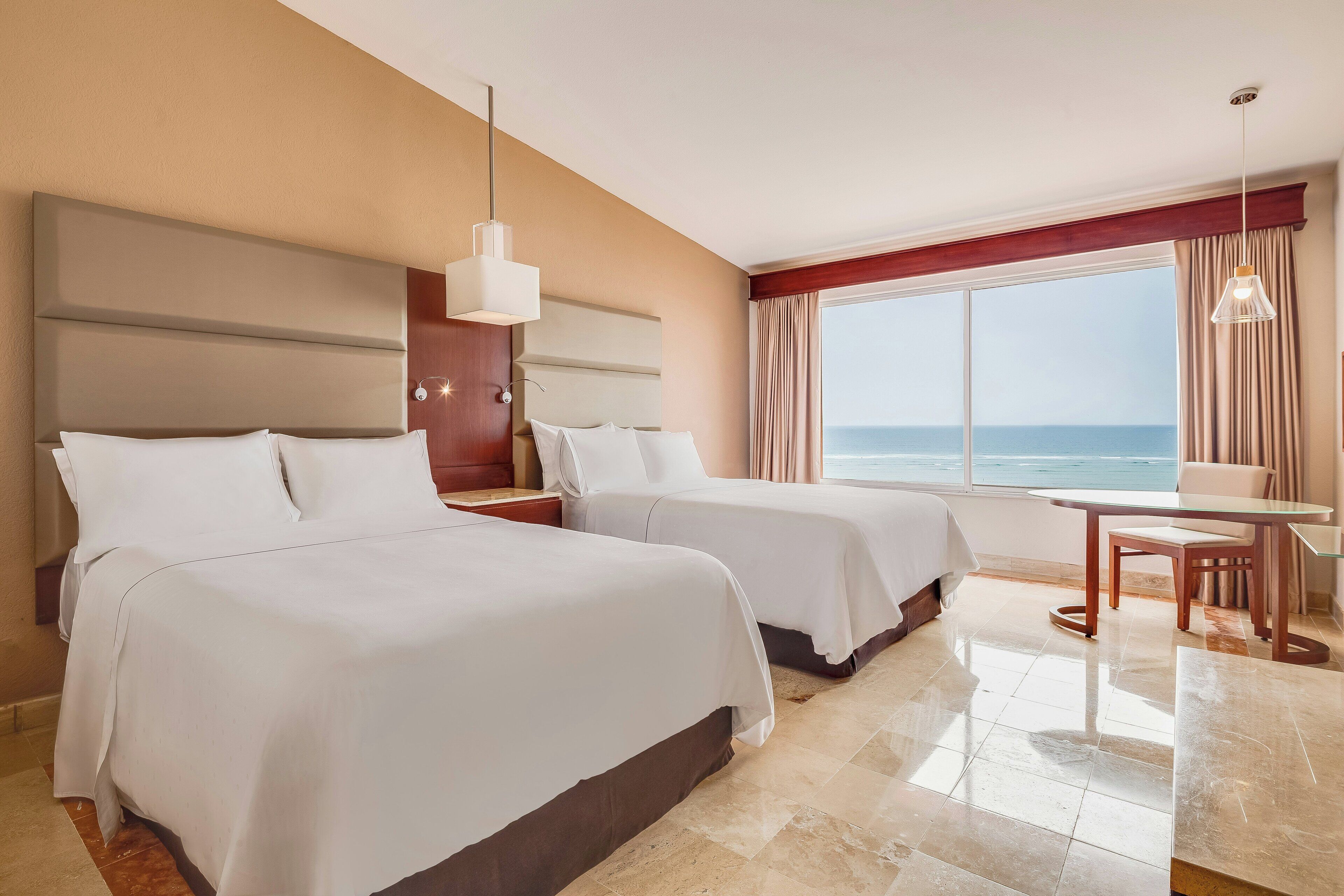 Une chambre d’hôtel avec deux lits, une table à manger et vue sur la mer.
