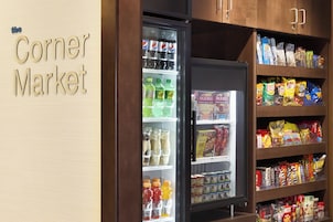Un mercado de barrio con una vitrina refrigerada y estantes llenos de aperitivos y bebidas.