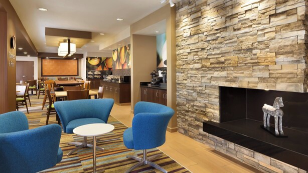 A modern hotel lobby with a stone fireplace, blue armchairs, a dining area, and a kitchen in the background. - Fairfield Inn & Suites Colorado Springs Air Force Academy (Colorado Springs)