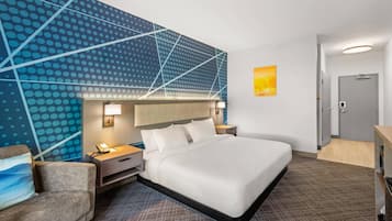 A hotel room with a large bed, a desk, a chair, a nightstand, a wall with a geometric pattern, and a door.