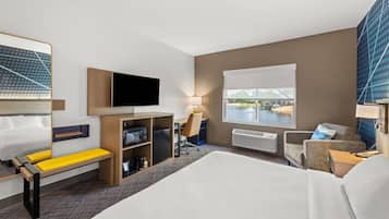 A hotel room with a bed, a desk, a television, a window with a view, and a seating area.