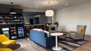 Un espacio de sala moderno con sofá, sillas, una mesa de centro y un refrigerador lleno de refrigerios.