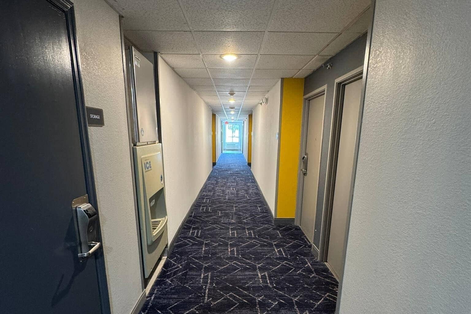 Corredor de hotel com carpete estampado, um armário e uma porta com puxador.