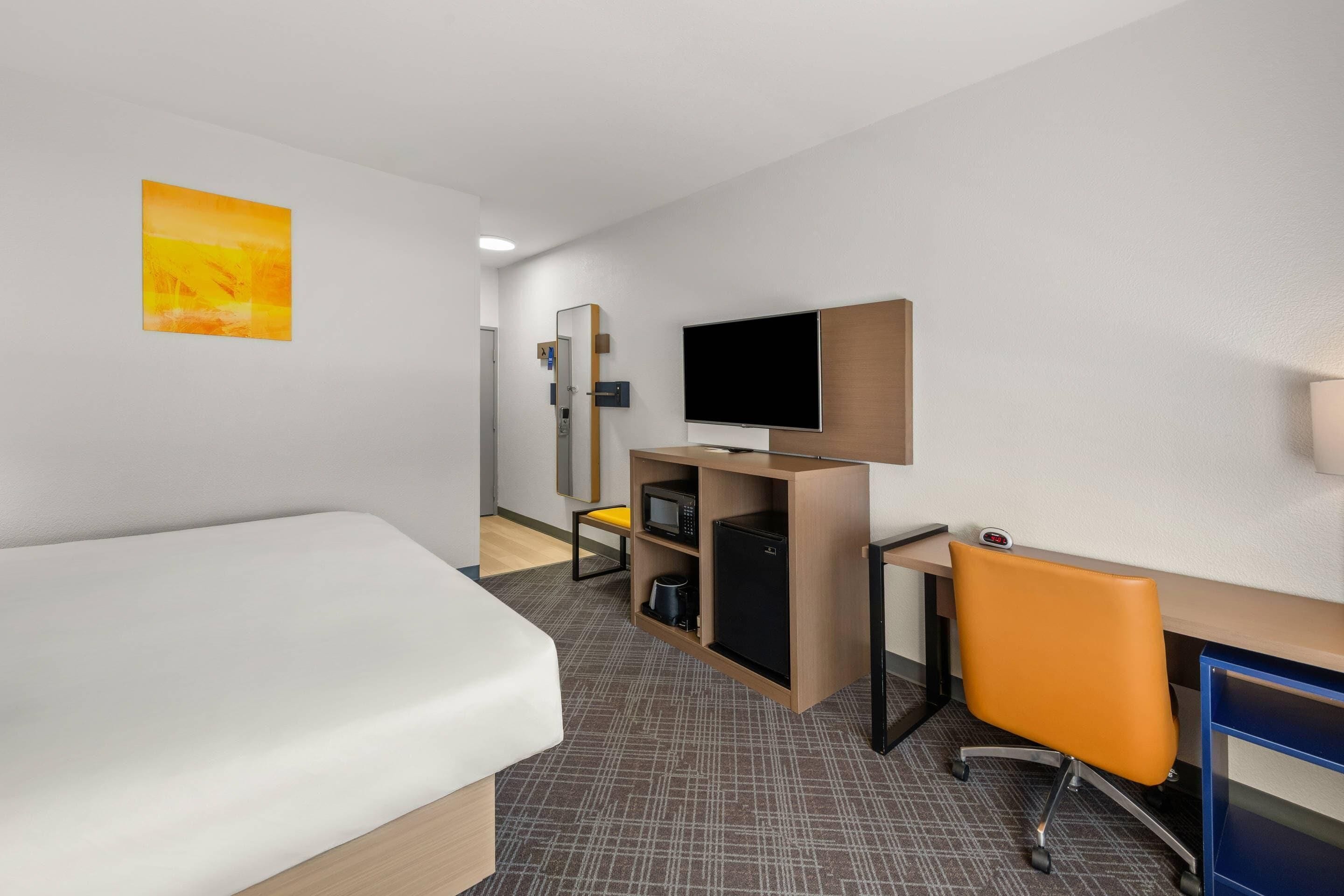 A hotel room with a bed, desk, chair, television, microwave, and a small refrigerator.