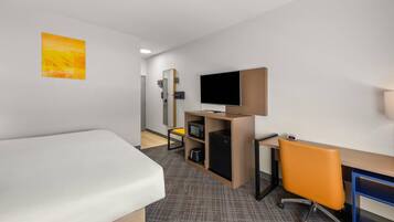 Ein Hotelzimmer mit Bett, Schreibtisch, Stuhl, Fernseher, Mikrowelle und kleinem Kühlschrank.