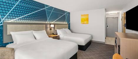 Hotellihuone, jossa on kaksi sänkyä, työpöytä, tuoli, televisio ja seinä, jossa on geometrinen kuvio.