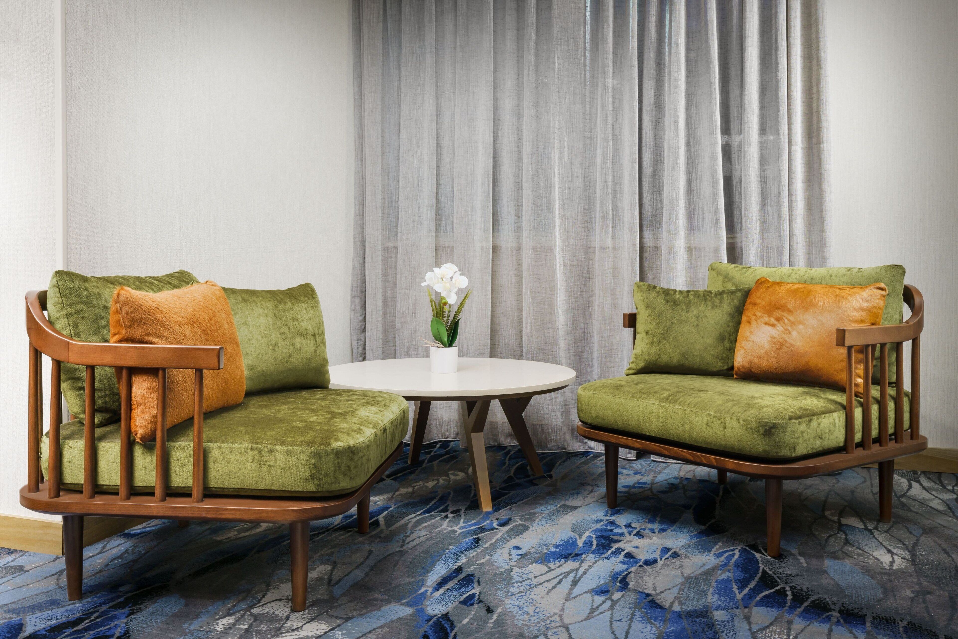 Una habitación con dos sillones verdes, una mesa redonda blanca y una orquídea en maceta.