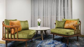 Una habitación con dos sillones verdes, una mesa redonda blanca y una orquídea en maceta.