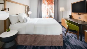 Habitación de hotel con una cama grande, un escritorio, una silla, un televisor y una ventana con cortinas.