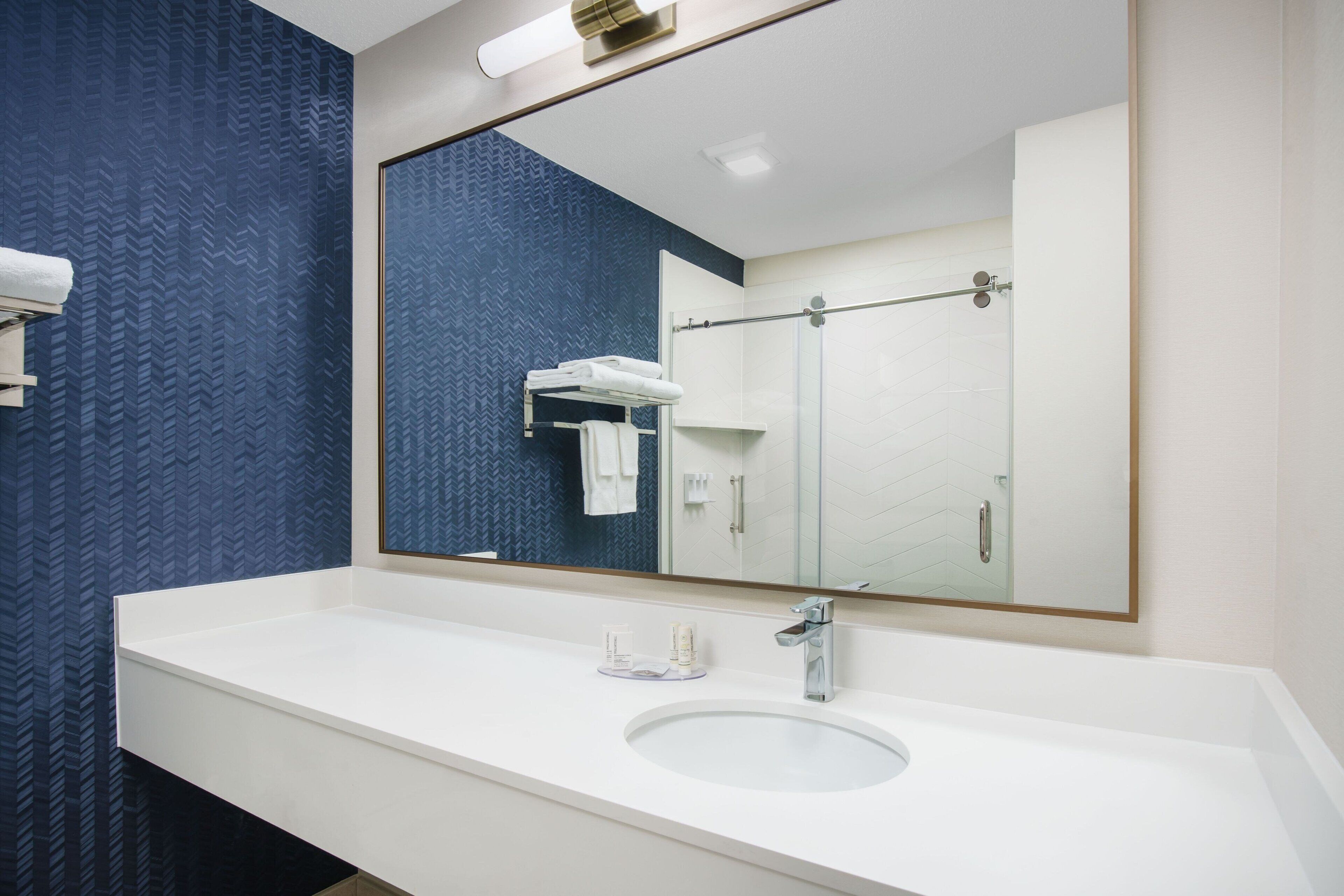 A modern bathroom with a white sink, a large mirror, and a glass shower enclosure.
