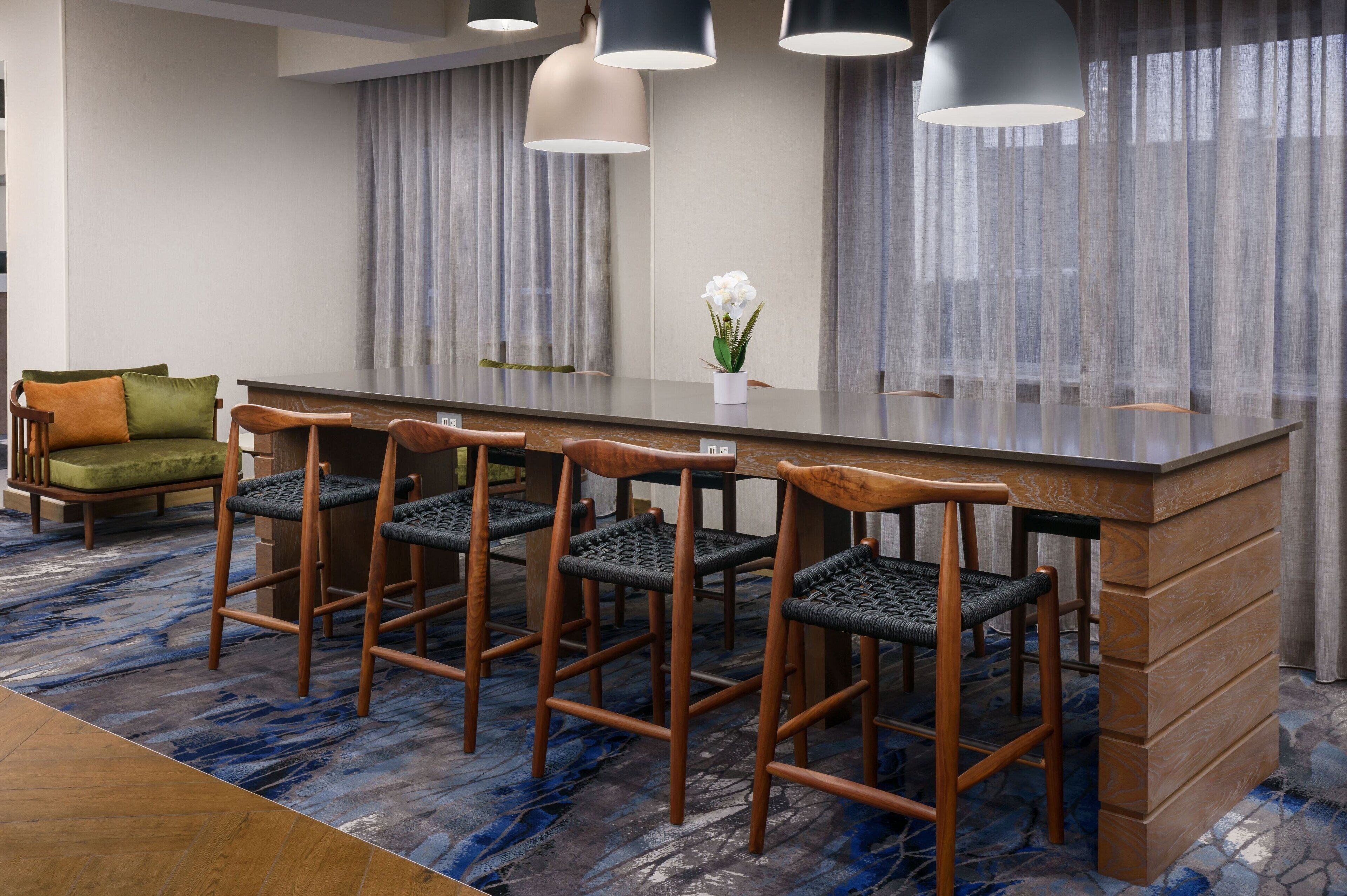 Habitación de hotel moderna con una barra central tipo isla, sillas de madera, un sofá con cojines y una alfombra estampada.