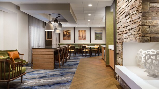Un hall de hotel con una zona de estar con banca de madera, un mostrador de recepción y una pared decorativa de piedra.