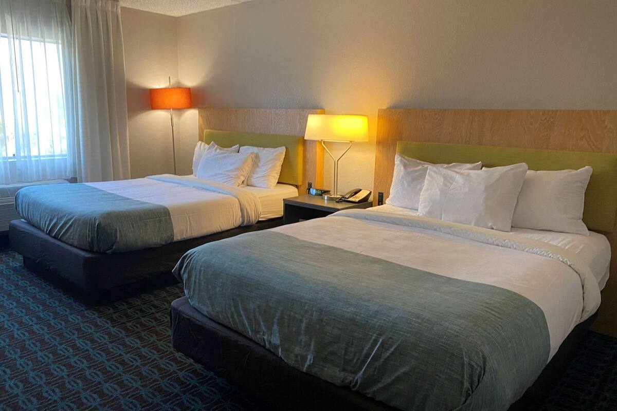 A hotel room with two beds, a nightstand with a lamp, and a window with curtains.