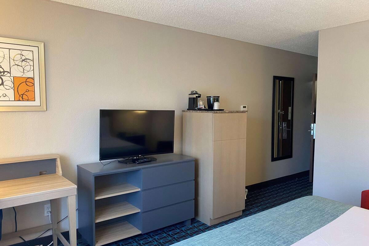 A hotel room with a bed, a desk, a television, a wardrobe, and a coffee maker.