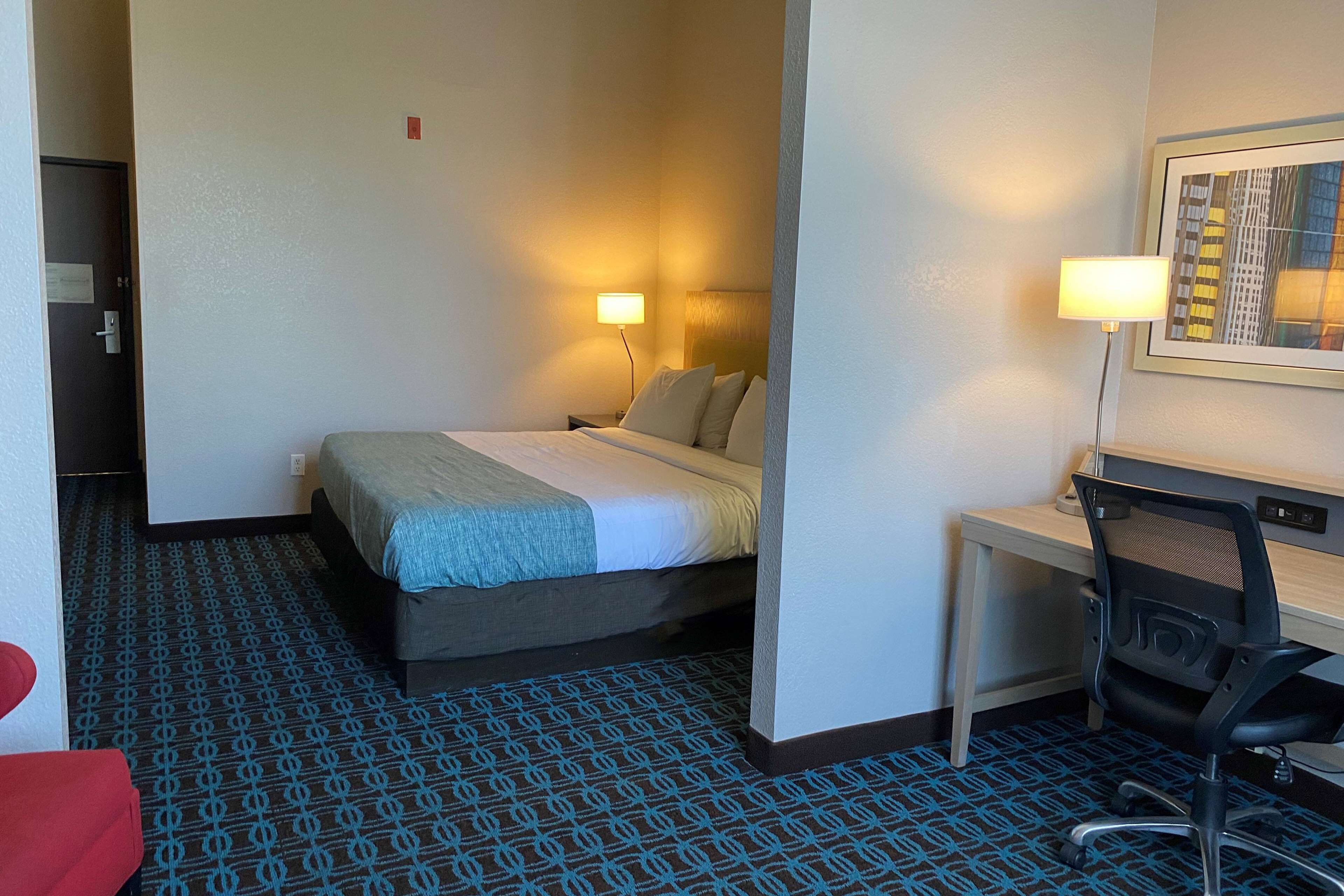 Hotellihuone, jossa on sänky, työpöytä, tuoli ja seinään kiinnitetty valaisin.