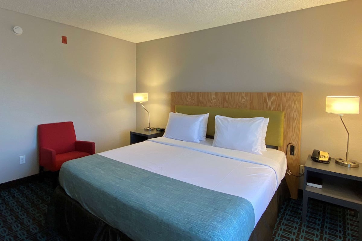 A hotel room with a large bed, a red chair, two bedside tables with lamps, and a patterned carpet.