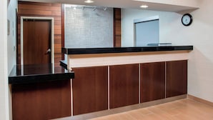 Zona de recepción con pared de paneles de madera, mostrador negro y un reloj en la pared.