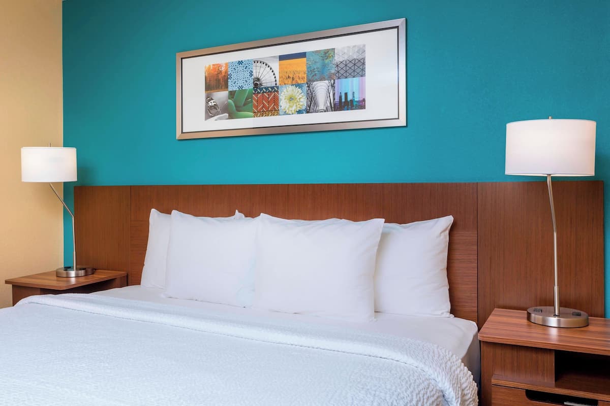 A hotel room with a large bed, white bedding, a teal accent wall, and a framed artwork above the bed.