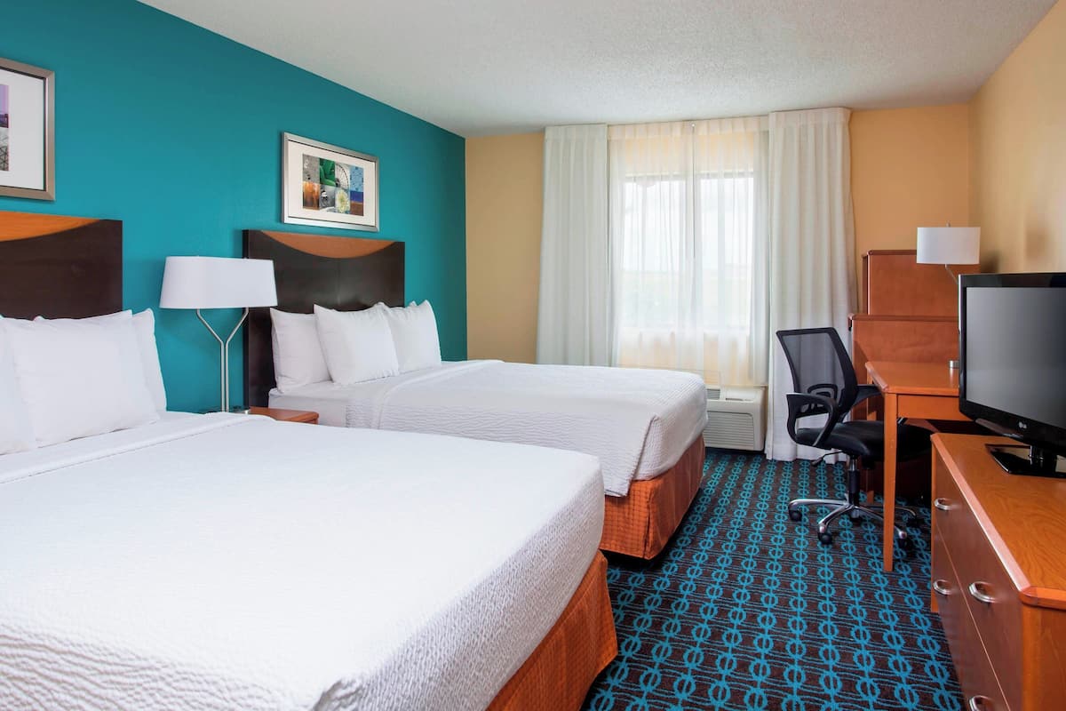 A hotel room with two beds, a desk with a television, and a chair.
