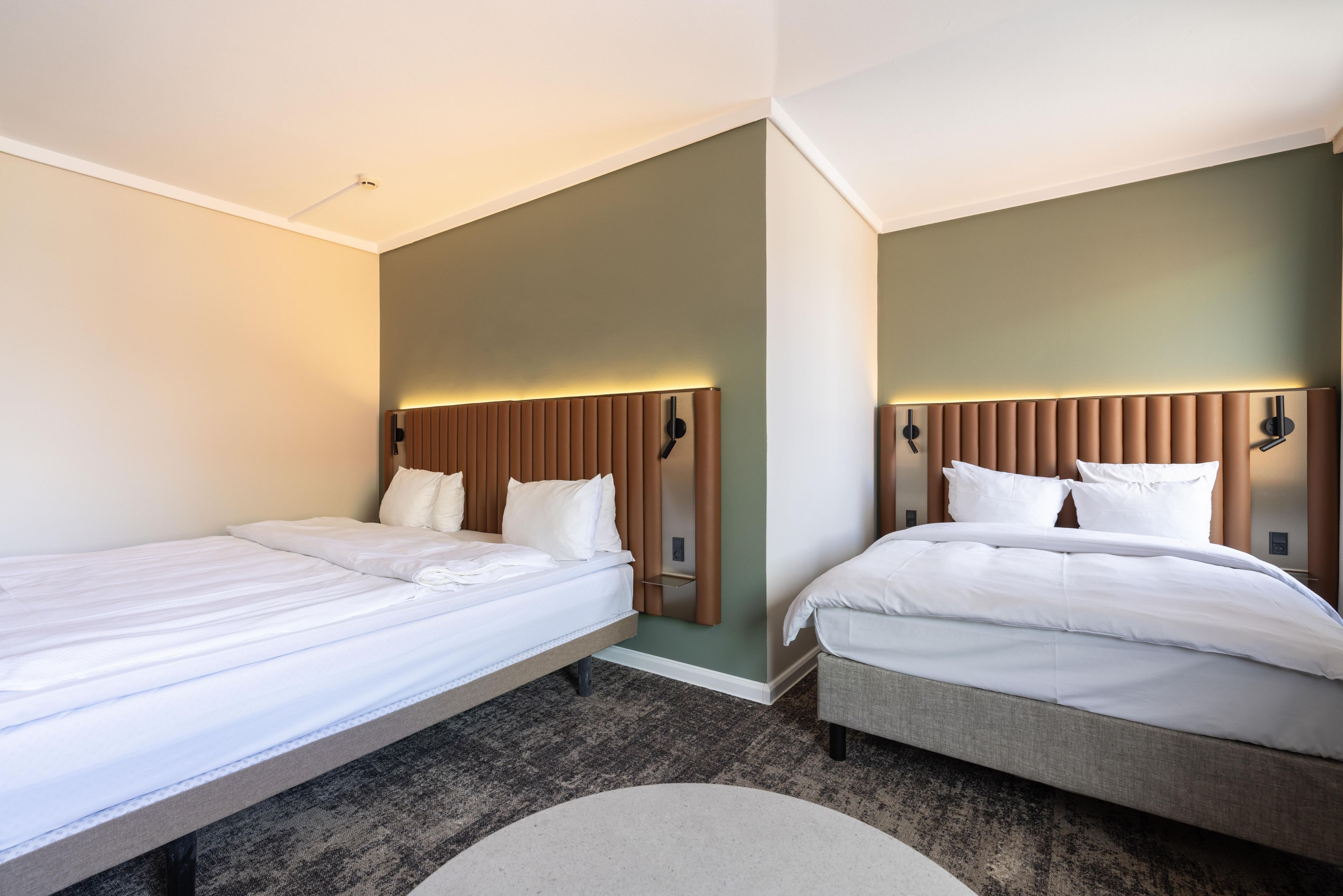 A hotel room with two single beds, a small round table, and a wall-mounted clock.