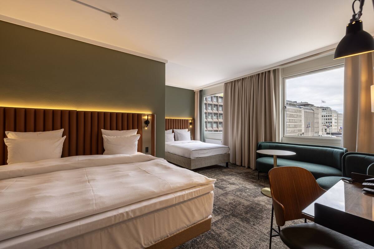 A hotel room with two beds, a sofa, a small table, and a view of the city.