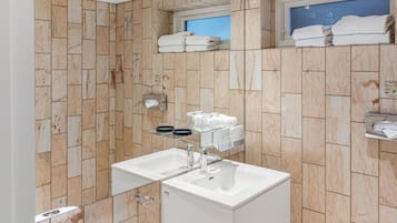 A bathroom with marble walls, two sinks, a glass shelf with toiletries, and a towel rack with folded towels.