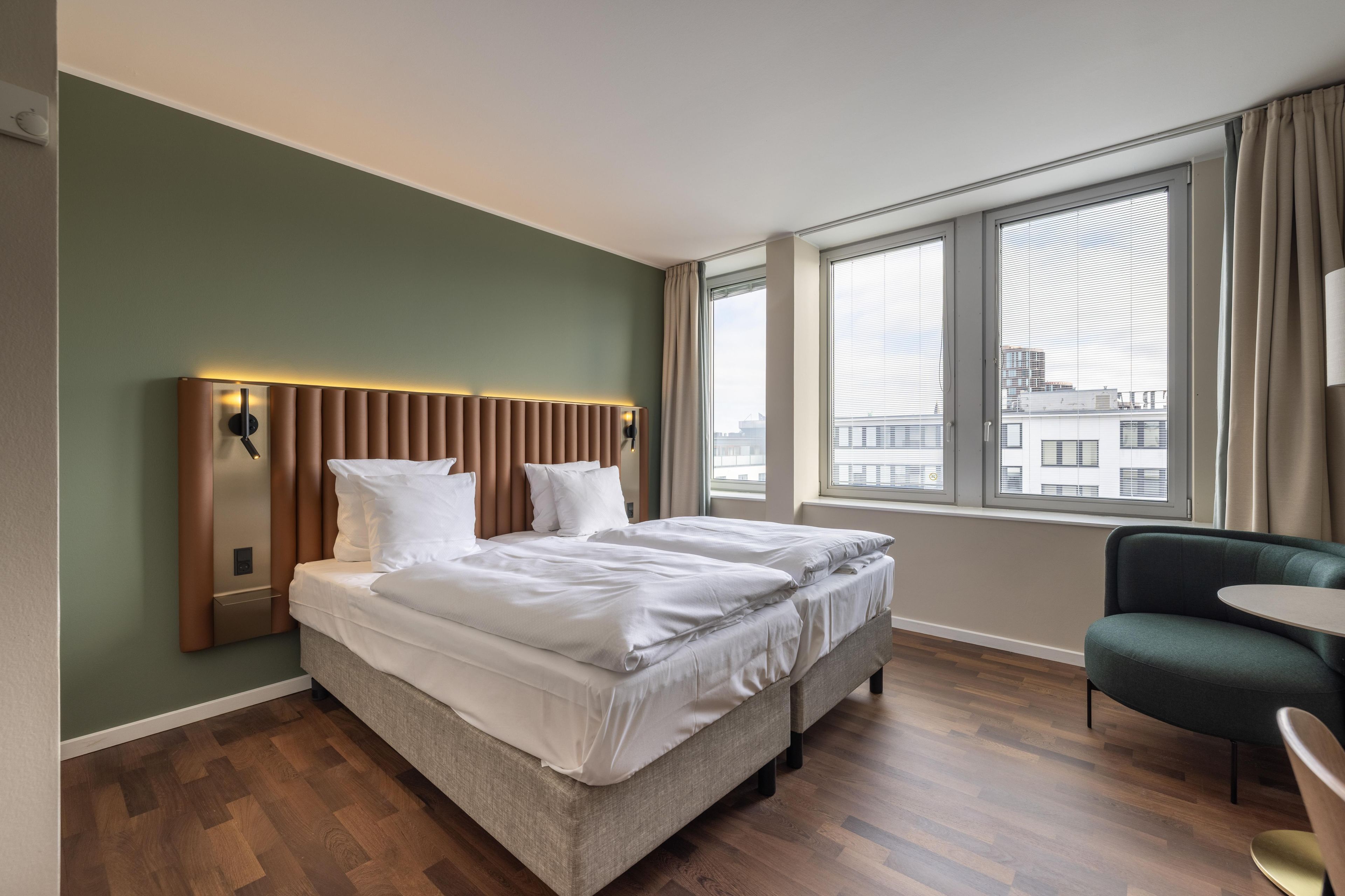 A hotel room with a bed, a chair, and a window with a view of buildings.