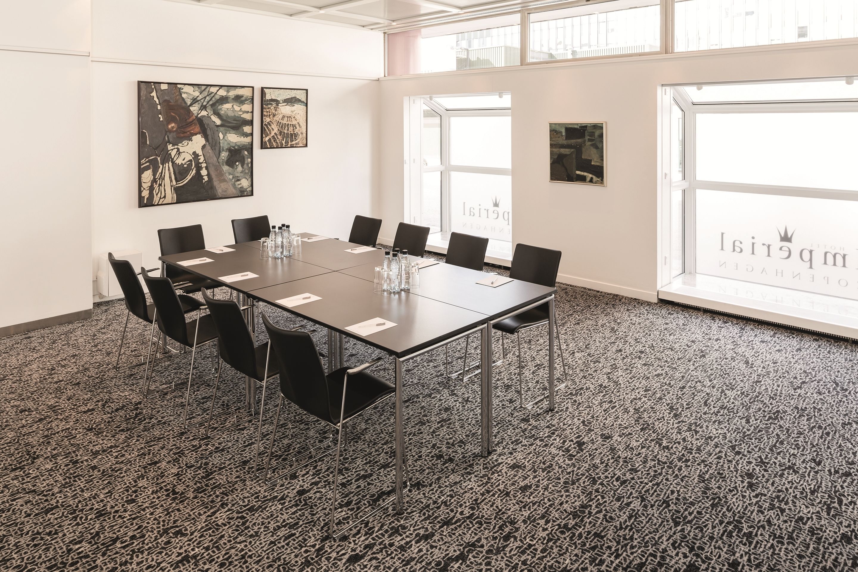 A conference room with a long table, black chairs, and a patterned carpet.