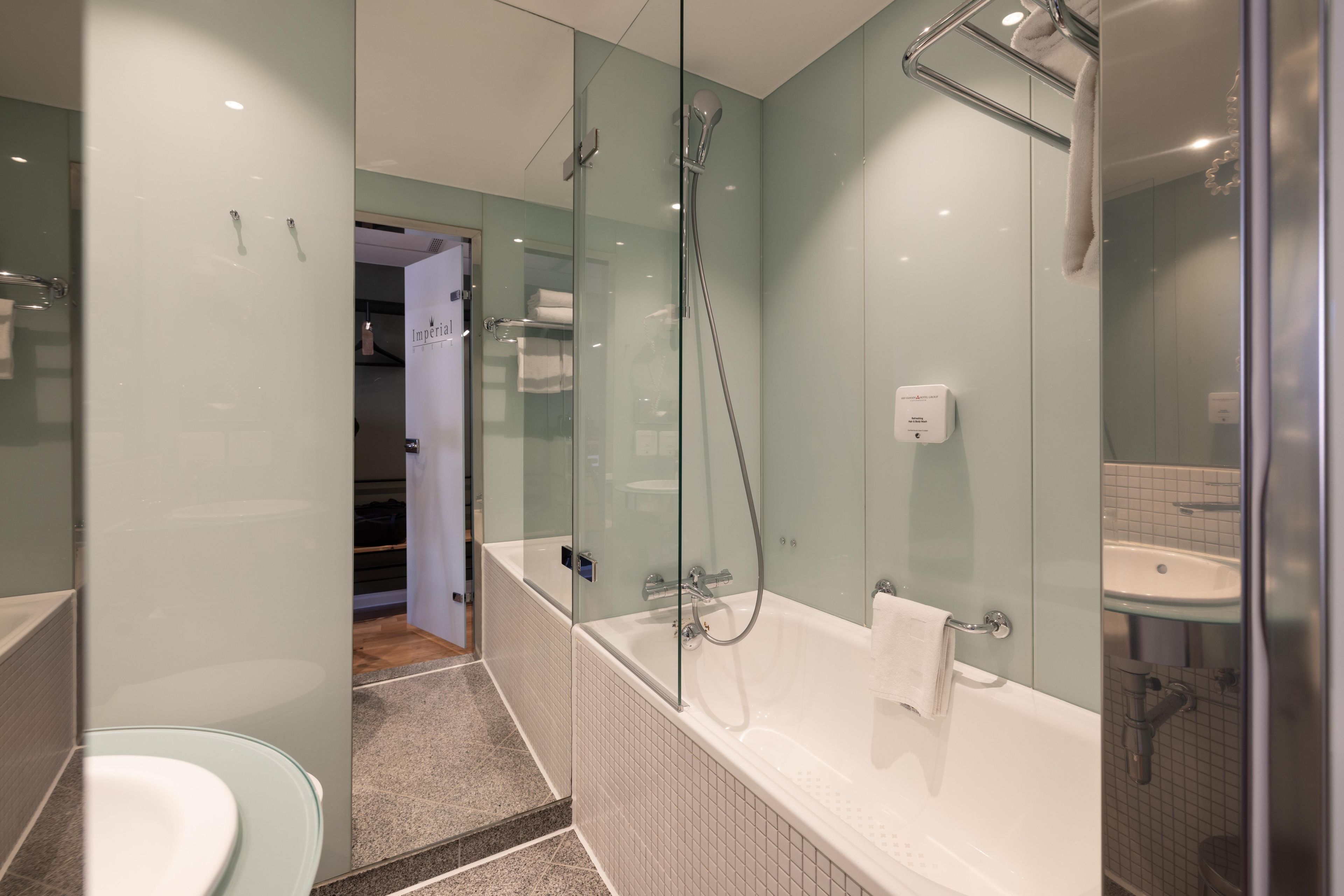 Un baño moderno con ducha envuelta en vidrio, bañera blanca y lavamanos de vidrio.