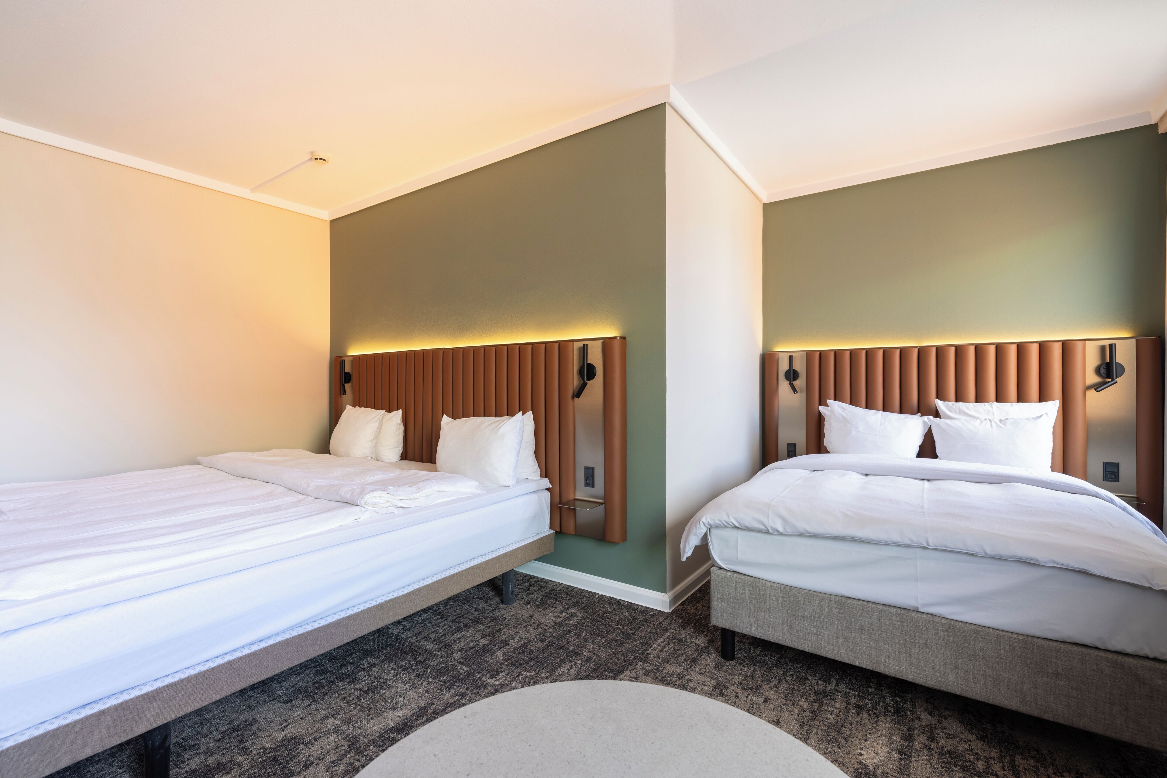 A hotel room with two single beds, a small bedside table, and a large round rug.